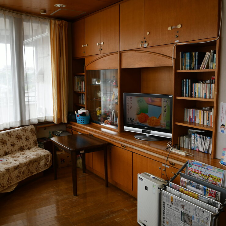 木製家具とテレビを備えた居室の共用スペース。図書棚と談話エリア。