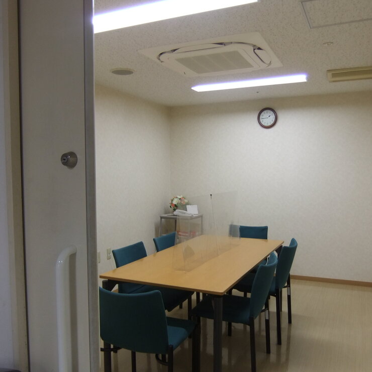 介護施設の会議室・談話室。木製テーブルと青い椅子が配置された明るい共用スペース
